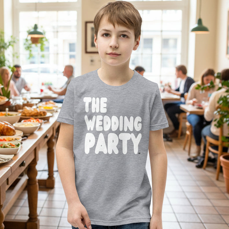 Boy standing at a breakfast buffet wearing the APWT Gift Shop's The Wedding Party Kids Unisex T-Shirt from the APWT Wedding Shop in Grey