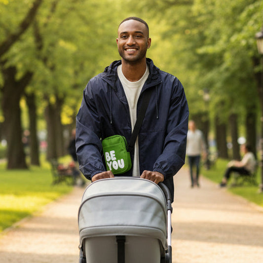 Man pushing a baby in stroller in a park wearing the APWT Gift Shop's Be You in Green Small Crossbody Bag from the Be You Collection