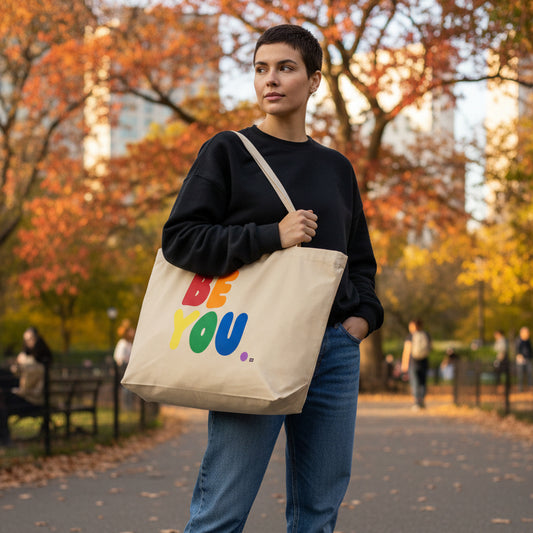Woman walking in a city park carrying the APWT Gift Shop's Rainbow Be You Jumbo Tote Bag from the Be You Community and the Pride in the APWT Gift Shop Collection