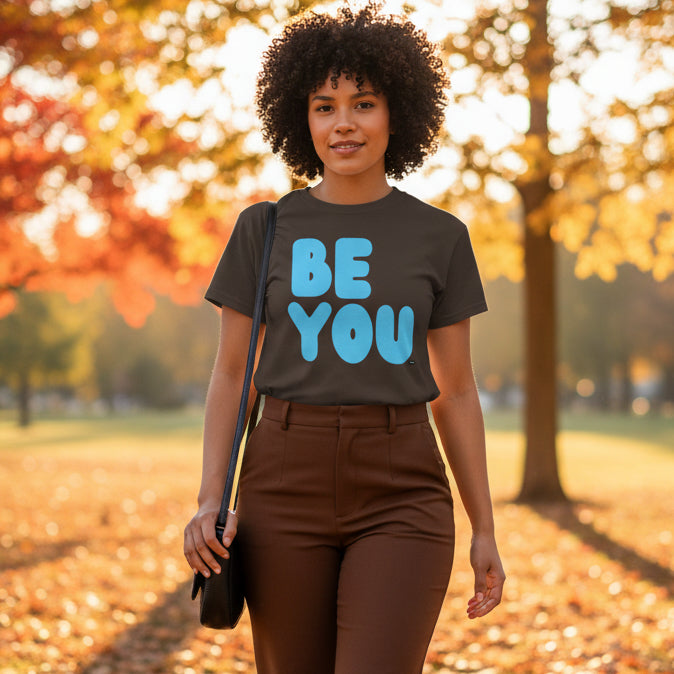 Woman walking through the park on an autumn day wearing the APWT Gift Shop's Be You in Brown and Blue Unisex T-Shirt from the Be You Collection