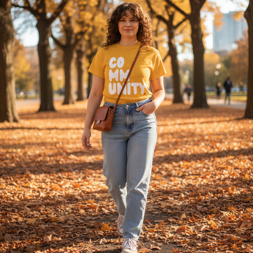 Woman walking through the park on an autumn day wearing the APWT Gift Shop's A Community in Sunflower Yellow Unisex T-Shirt from the Community Collection