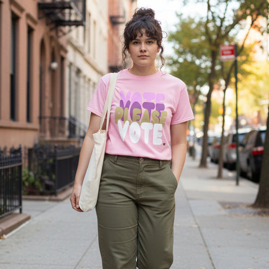 Woman walking down a city street wearing the APWT Gift Shop's Please Vote in Primaries Pink Unisex T-Shirt from the APWT Vote Shop