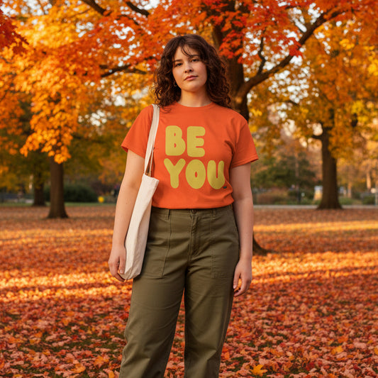 Woman standing in the park on an autumn day wearing the APWT Gift Shop's Be You in Orange and Yellow Unisex T-Shirt from the Be You Collection