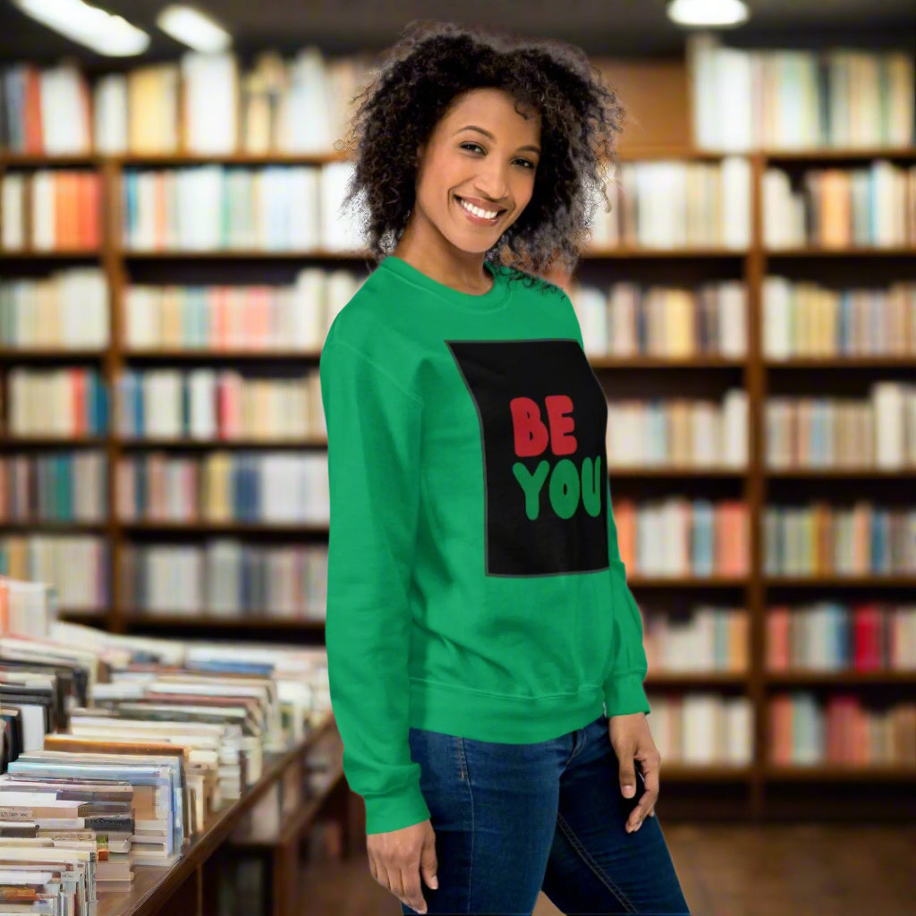 Woman wearing the Be You in Black Unisex Crew Neck Sweatshirt in Green standing in a library - The APWT Gift Shop