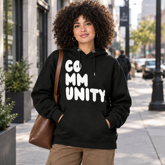 A woman standing on a city sidewalk wearing the APWT Gift Shop's A Community in Black and White Premium Unisex Hoodie from the Premium Basics Collection and the Community Collection