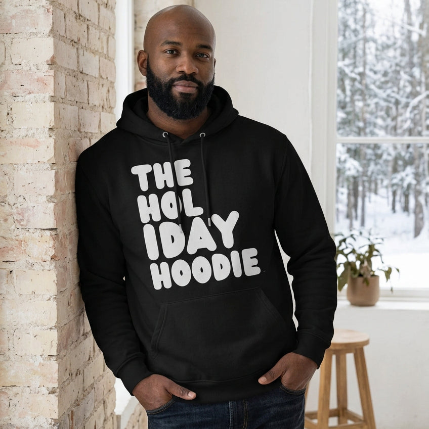 Man standing in a white room wearing The APWT Gift Shop's The Holiday Celebration Premium Unisex Hoodie from the APWT Holiday Shop and the Day in the Life Collection