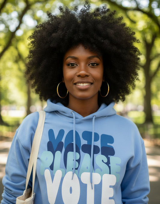 Woman walking through a city park wearing the APWT Gift Shop's Please Vote in Sky Blue Unisex Hoodie from the APWT Vote Shop