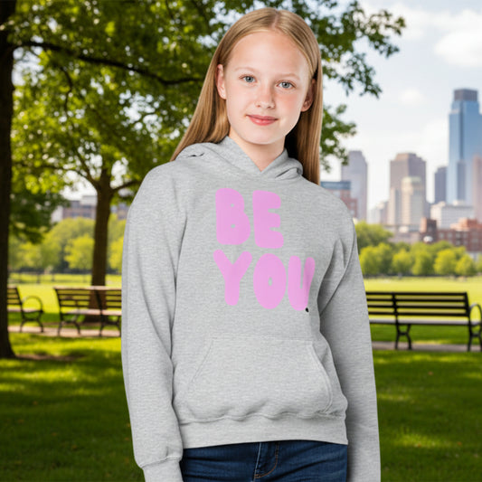 Girl in park wearing Be You Kids in Pink Unisex Hoodie in Grey from the APWT Gift Shop - Kids Affirmation Sweatshirts