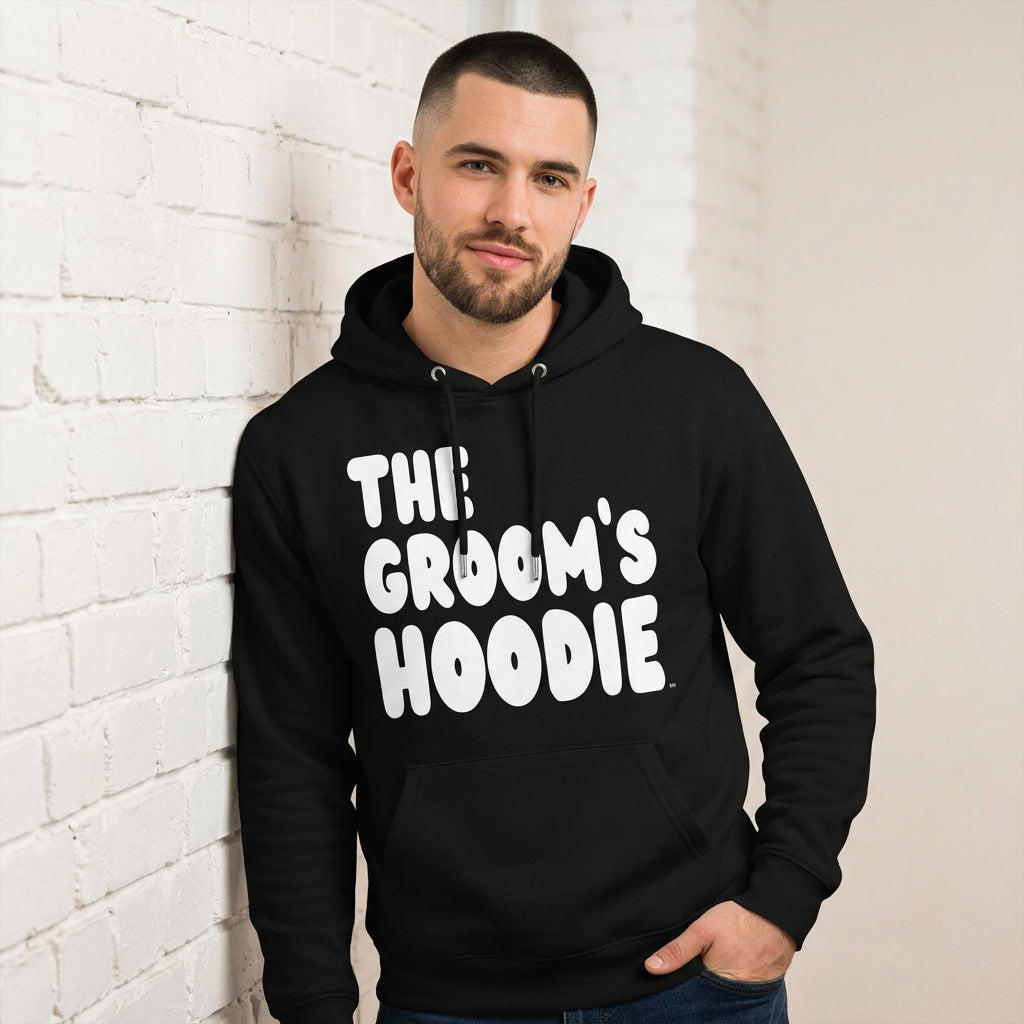 Man wearing the Groom's Hoodie Premium Unisex Hoodie From the APWT Wedding Shop in Black