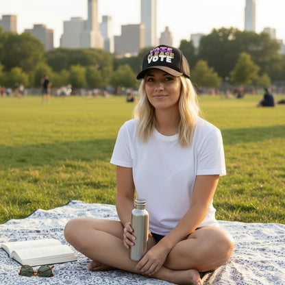Woman sitting in the park wearing the APWT Gift Shop's Please Vote in Pink Trucker Hat from the APWT Vote Shop
