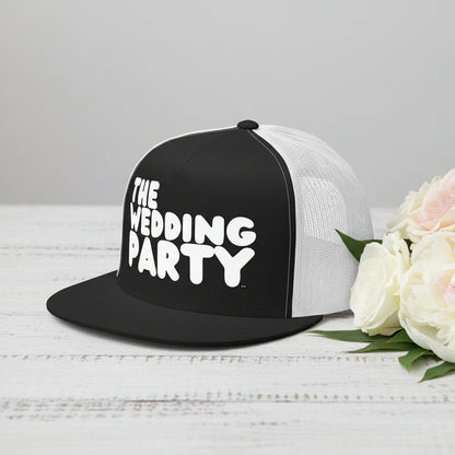 The APWT Gift Shop's The Wedding Party Trucker Hat from the APWT Wedding Shop in Black/White sitting on a  white wooden table next to flowers