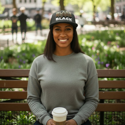 Woman sitting in the park on a bench wearing the APWT Gift Shop Shades in Black Trucker Hat in charcoal grey featuring the word 'Black' in different shades of brown