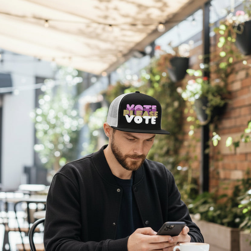 Man sitting at a cafe wearing the APWT Gift Shop's Please Vote in Pink Trucker Hat from the APWT Vote Shop