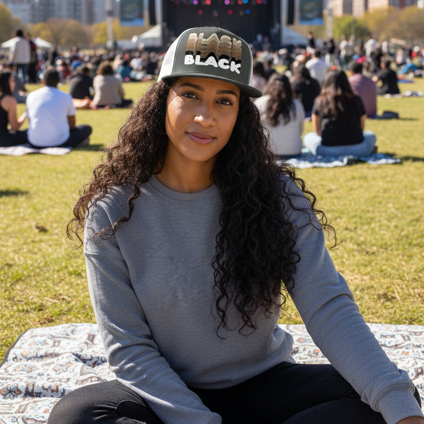 Woman sitting in the park on a blanket wearing the APWT Gift Shops Shades in Black Trucker Hat in Charcoal Grey and White