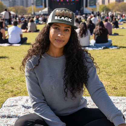 Woman sitting in the park on a blanket wearing the APWT Gift Shops Shades in Black Trucker Hat in Charcoal Grey and White