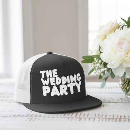 The APWT Gift Shop's The Wedding Party Trucker Hat from the APWT Wedding Shop in Charcoal/White sitting on a  white wooden table next to flowers