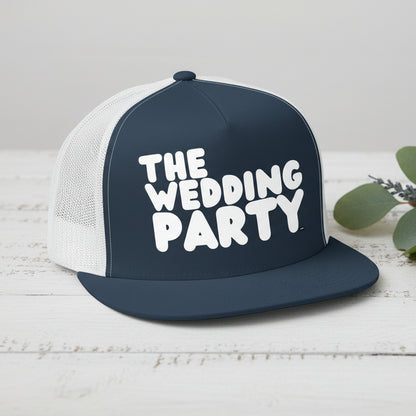 The APWT Gift Shop's The Wedding Party Trucker Hat from the APWT Wedding Shop in Navy Blue/White sitting on a  white wooden table next to flowers