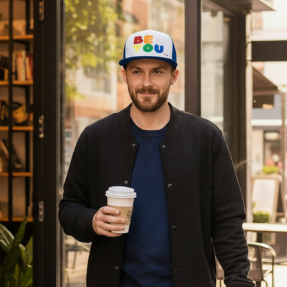 Man walking down the street carrying a cup of coffee wearing the APWT Gift Shop's Rainbow Be You Trucker Hat from the Pride in the APWT Gift Shop Collection and the Be You Collection in Royal Blue and white