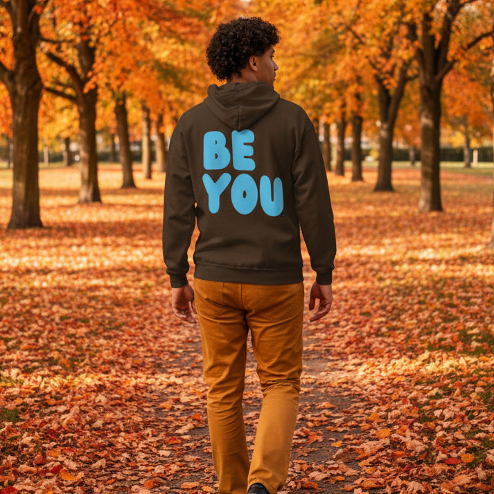 Man walking through the park on an autumn day wearing the APWT Gift Shop's Be You in Brown and Blue Unisex Zip-Up Hoodie from the Be You Collection