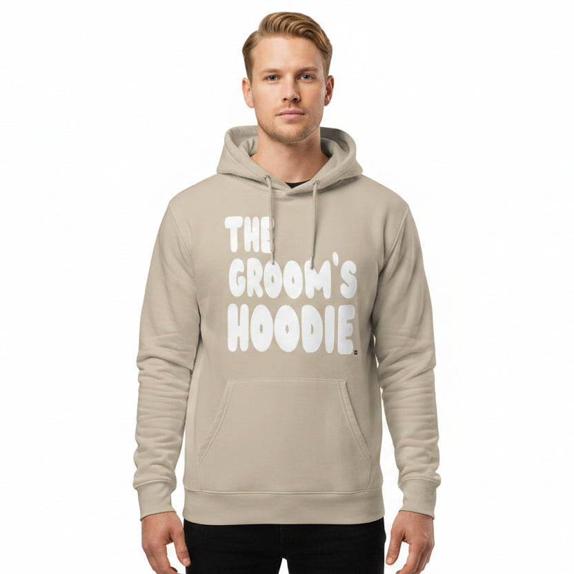 Man wearing the APWT Gift Shop's The Groom's Hoodie Premium Unisex Hoodie from the APWT Wedding Shop in Beige