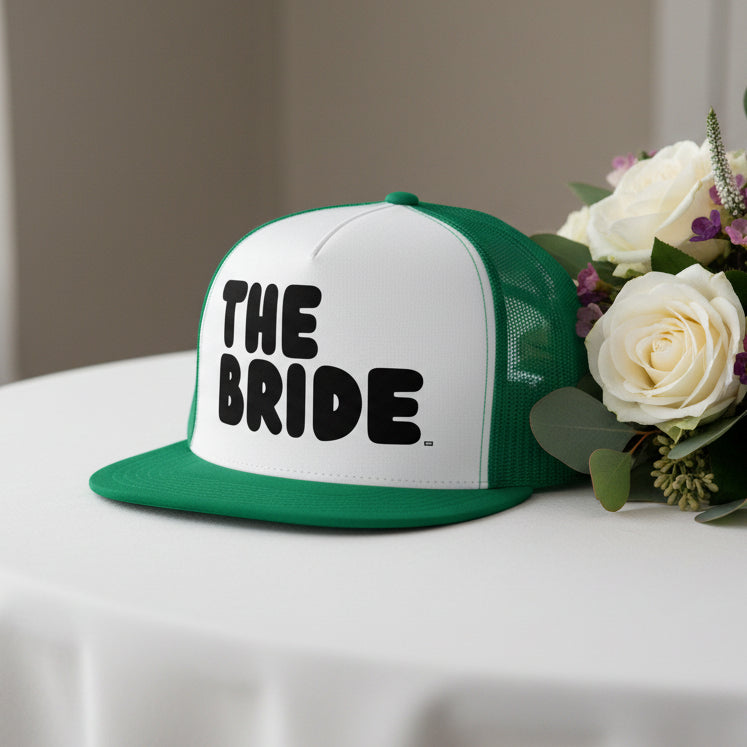 The Bride Trucker Hat from the APWT Gift Shop in Green and White on a table
