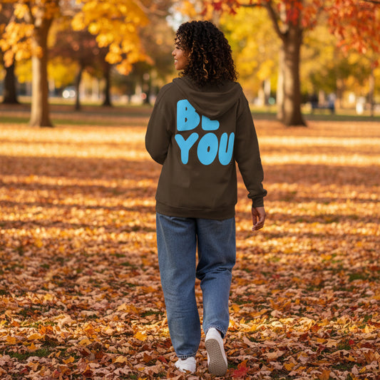 Woman walking through the park on an autumn day wearing the APWT Gift Shop's Be You in Brown and Blue Unisex Zip-Up Hoodie from the Be You Collection