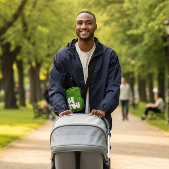 Man pushing a baby in stroller in a park wearing the APWT Gift Shop's Be You in Green Small Crossbody Bag from the Be You Collection