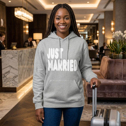 Woman standing in a hotel lobby wearing the APWT Gift Shop's Just Married Premium Unisex Hoodie from the APWT Wedding Shop and the Premium Basics Collection in grey