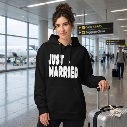 Woman standing in an airport wearing the APWT Gift Shop's Just Married Premium Unisex Hoodie from the APWT Wedding Shop and the Premium Basics Collection in black