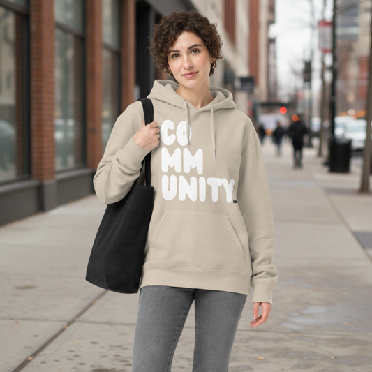 Man standing on a city street wearing the APWT Gift Shop's A Community in Beige and White Premium Unisex Hoodie from the Community Collection and the Premium Basics Collection