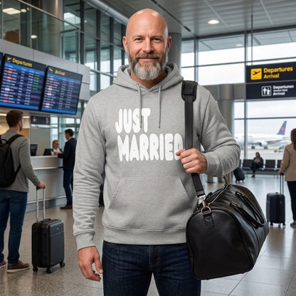 Man standing in an airport wearing the APWT Gift Shop's Just Married Premium Unisex Hoodie from the APWT Wedding Shop and the Premium Basics Collection in grey