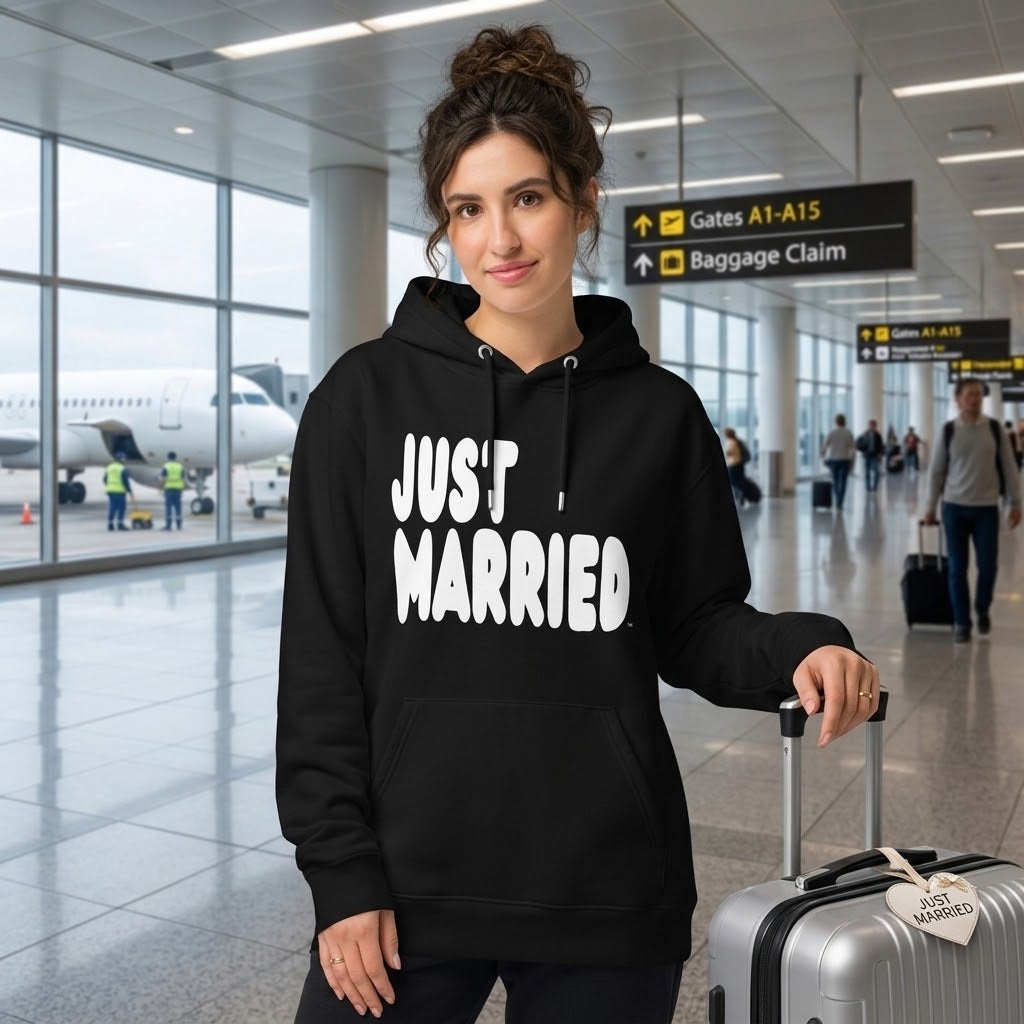 Woman standing in an airport wearing the APWT Gift Shop's Just Married Premium Unisex Hoodie from the APWT Wedding Shop and the Premium Basics Collection in black
