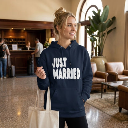 Woman standing in a hotel lobby wearing the APWT Gift Shop's Just Married Premium Unisex Hoodie from the APWT Wedding Shop and the Premium Basics Collection in navy blue