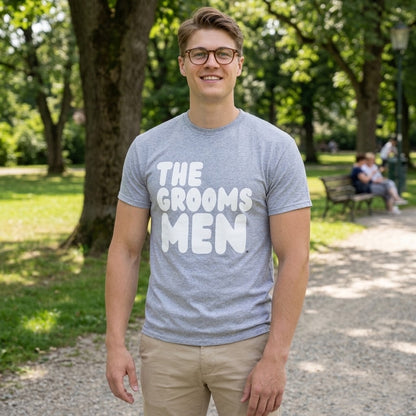 Man standing in a park wearing the APWT Gift Shop's the Groomsmen Unisex T-Shirt  from the APWT Wedding Shop and Day in the Life Collection in Grey