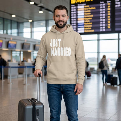 Man standing in an airport wearing the APWT Gift Shop's Just Married Premium Unisex Hoodie from the APWT Wedding Shop and the Premium Basics Collection in beige