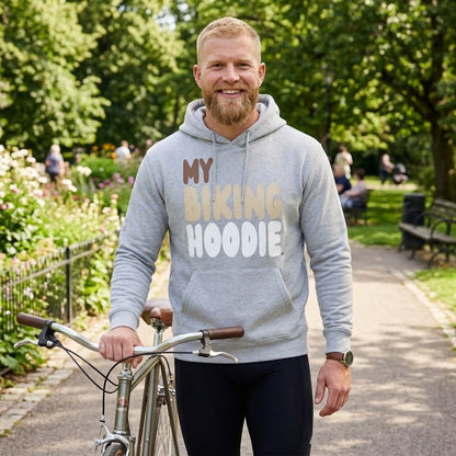 Man walking her bike through a park wearing the APWT Gift Shop's My Biking Hoodie Premium Unisex Hoodie from the Day in the Life Collection and the Premium Basics Collection in Grey