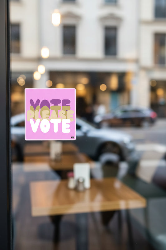 The APWT Gift Shop's Please Vote in Pink Vinyl Sticker from the APWT Vote Shop stuck to the outside window of a cafe