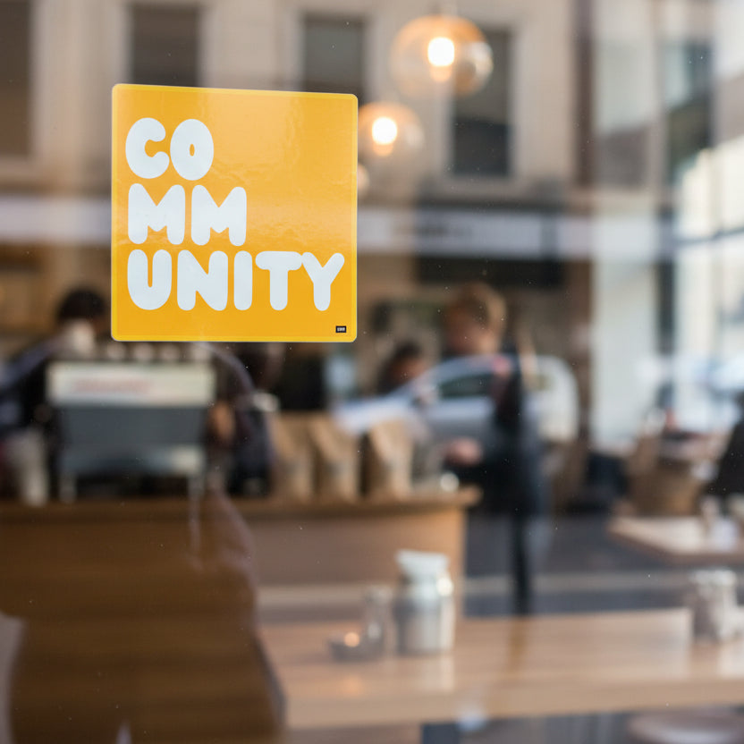 A Community in Sunflower Yellow Vinyl Sticker stuck to the outside window of  a coffee shop