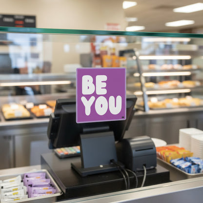 The APWT Gift Shop's Be You in Purple Sticker from the Be You Collection stuck the glass in front of  a cash register in a cafeteria