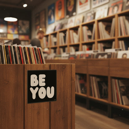 The APWT Gift Shop's Be You in Black and White Vinyl Sticker from the Be You Collection stuck to the side of crate holding records in a record shop