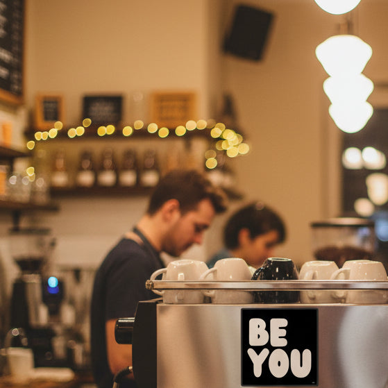 The APWT Gift Shop's Be You in Black and White Vinyl Sticker from the Be You Collection stuck to the side of a coffeemaker