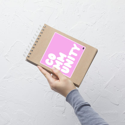 A Community in Pink Vinyl Sticker on a notebook - The APWT Gift Shop