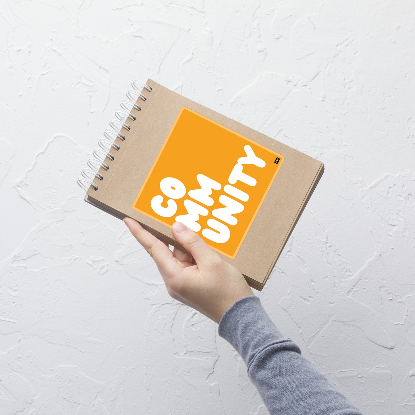 A Community in Orange Vinyl Sticker on a notebook - The APWT Gift Shop