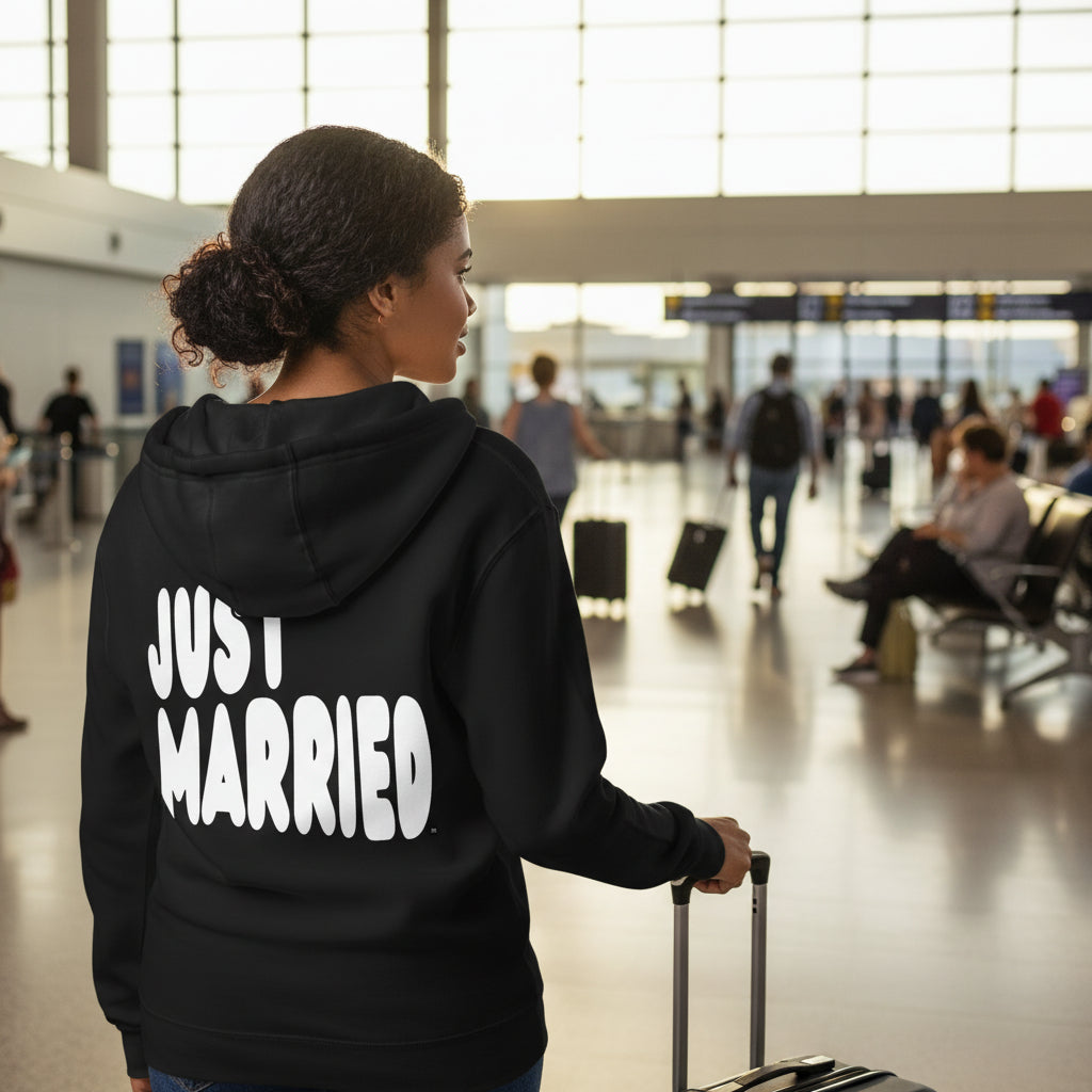 Woman standing in an airport wearing the APWT Gift Shop's Just Married Premium Unisex Zip-Up Hoodie in Black from the APWT Wedding Shop