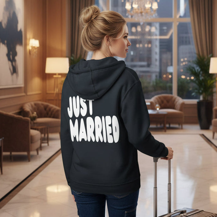Woman standing in a hotel lobby wearing the APWT Gift Shop's Just Married Premium Unisex Zip-Up Hoodie in Navy Blue from the APWT Wedding Shop
