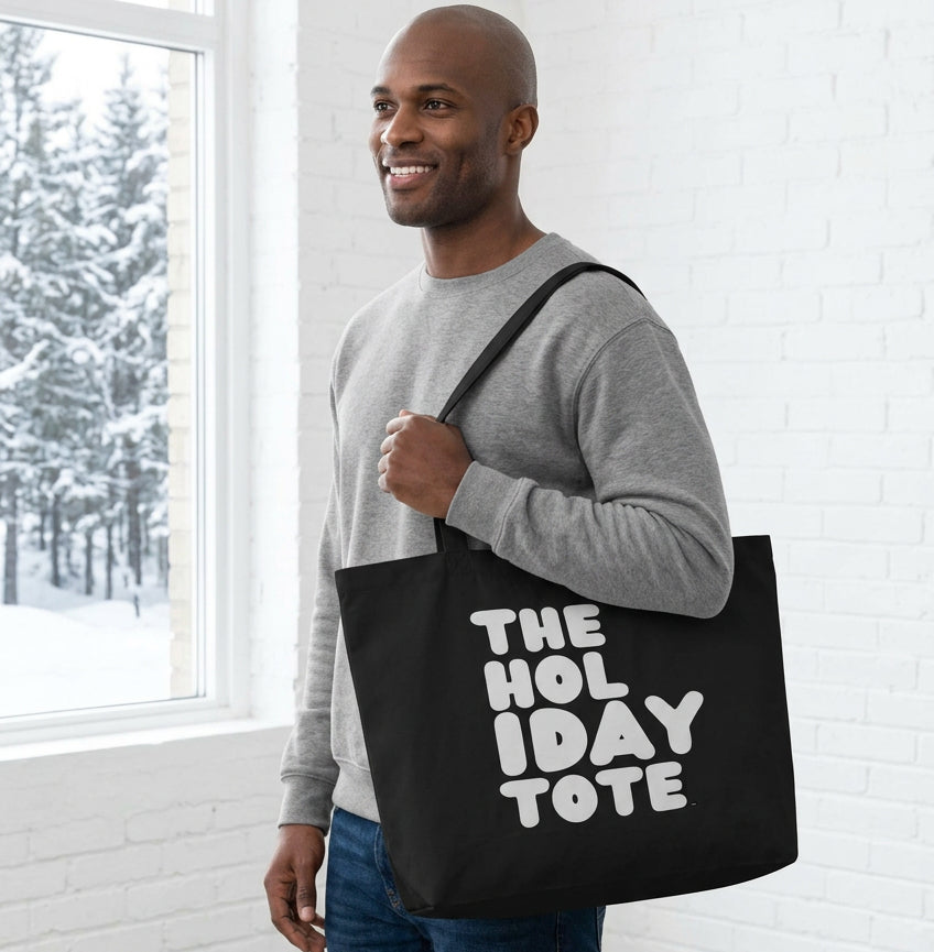 Man holding the APWT Gift Shop's The Holiday Celebration Jumbo Black Tote Bag from the APWT Holiday Shop and the Day in the Life Collection