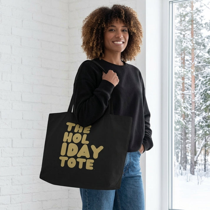 Woman holding the APWT Gift Shop's The Holiday Party Jumbo Black Tote Bag from the APWT Holiday Shop and the Day in the Life Collection
