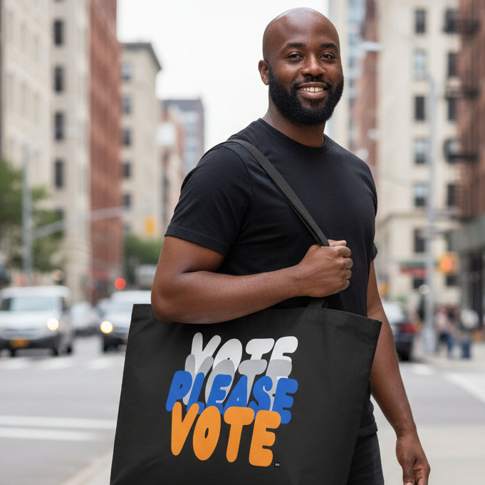 Man standing on a city street wearing The APWT Gift Shop's Please Vote in Blue and Orange Jumbo Tote Bag from the APWT Gift Shop in Black