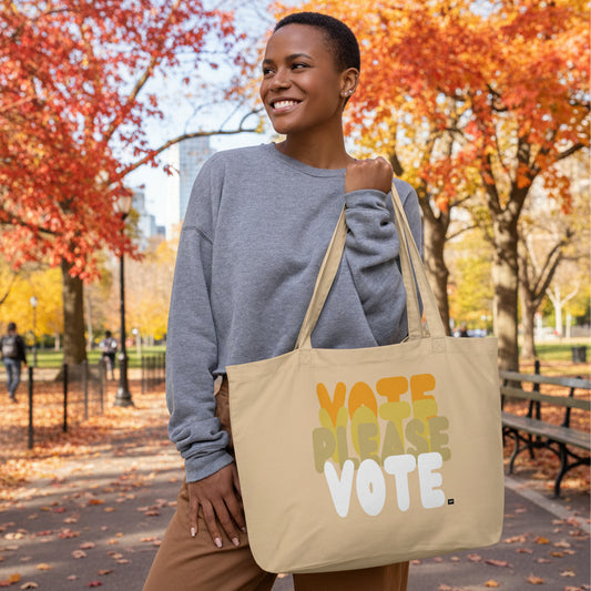 Woman standing in the park holding the APWT Gift Shop's Please Vote in Orange Jumbo Tote Bag from the APWT Vote Shop
