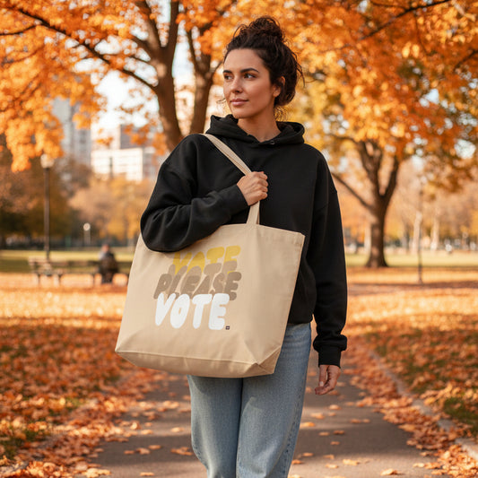 Woman walking through a city park carrying the APWT Gift Shop's Please Vote in Yellow Jumbo Tote Bag from the APWT Vote Shop